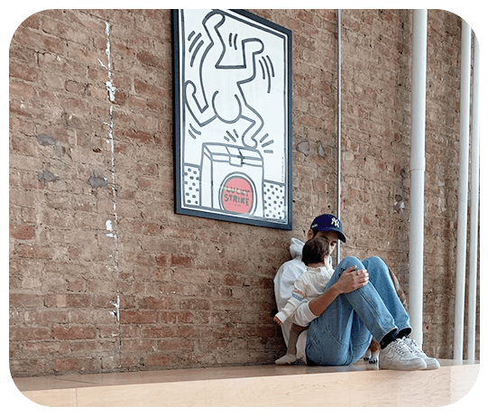Elliot Tebele, founder of FJerryLLC, sitting against a brick wall with artwork hanging on it.